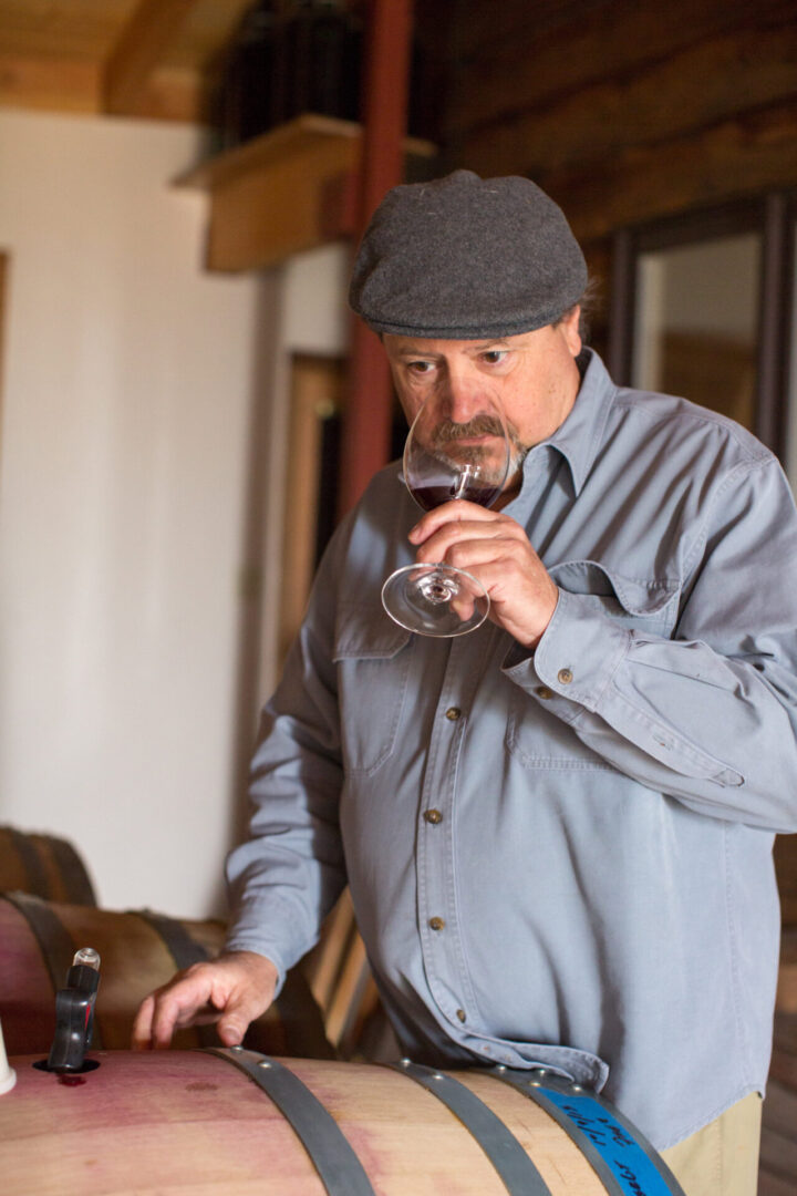 A man in grey shirt holding glass of wine.